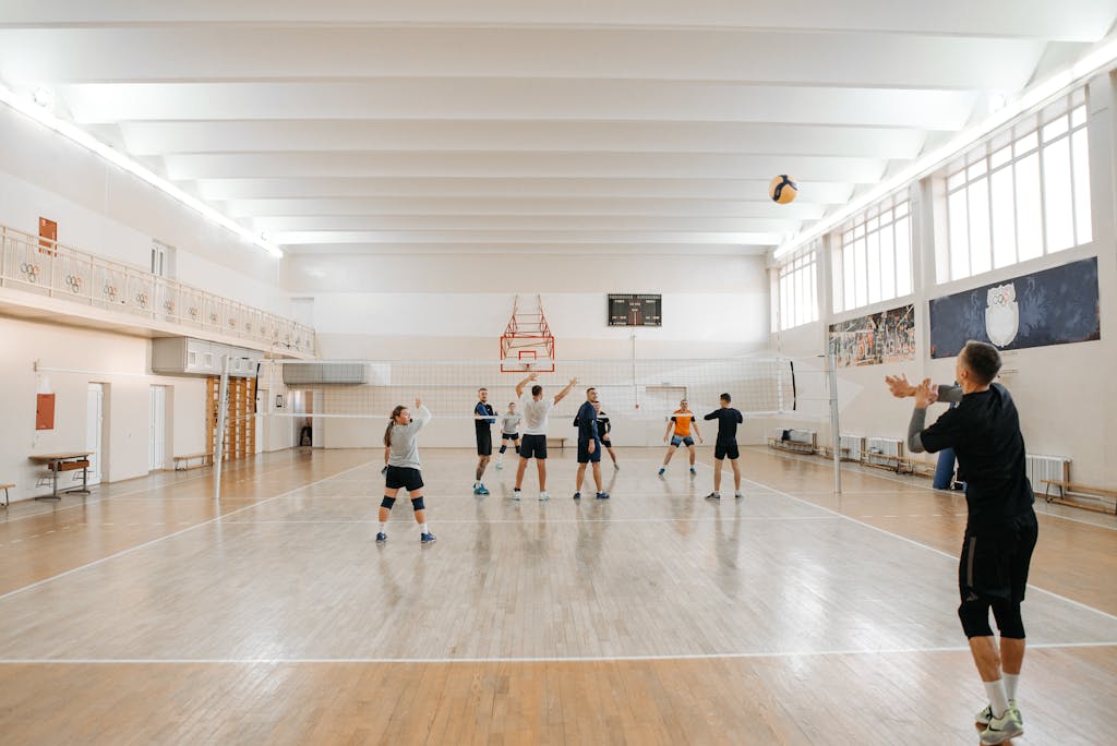 Adults energetically practicing volleyball indoors with a focus on teamwork.